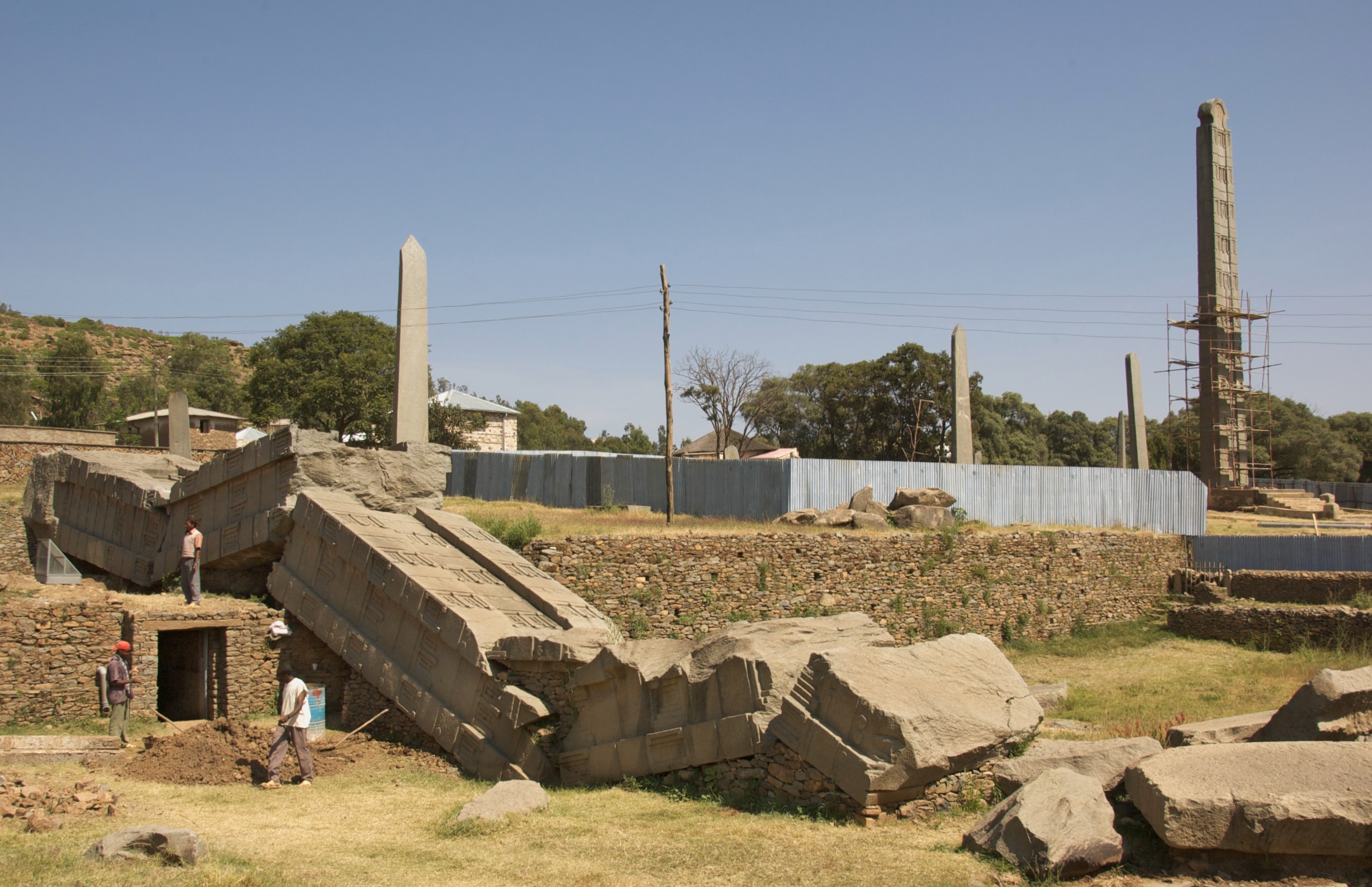 The broken Great Stela lying in sections in the foreground at Aksum, with tall standing stone stelae behind it