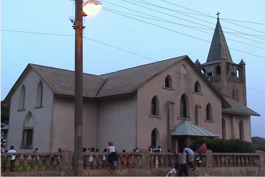 Christ Presbyterian Church in Akropong, Ghana, a large pale church with a pointed bell tower, at dusk