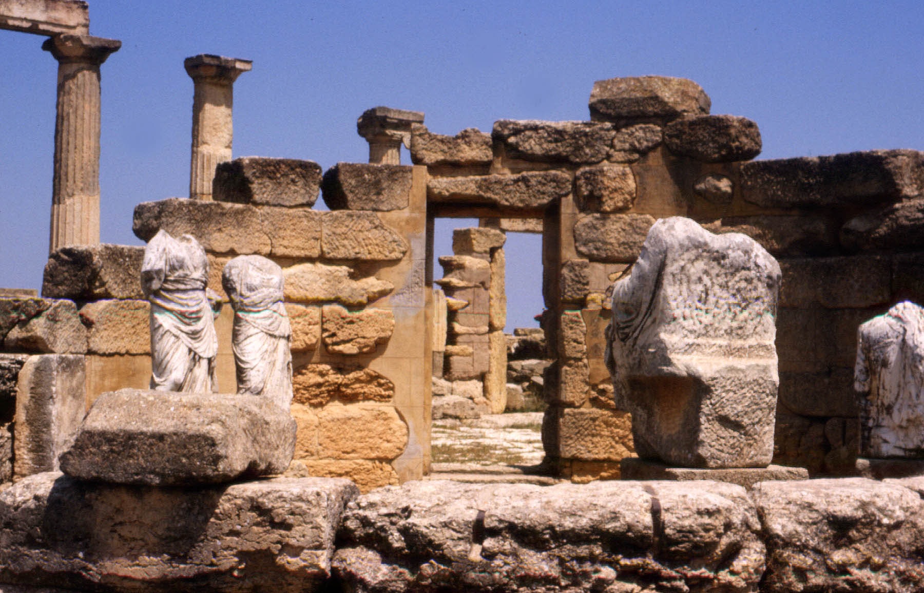 Ruined stone walls, a doorway and Doric columns with headless marble statues at the ancient Greek city of Cyrene in Libya
