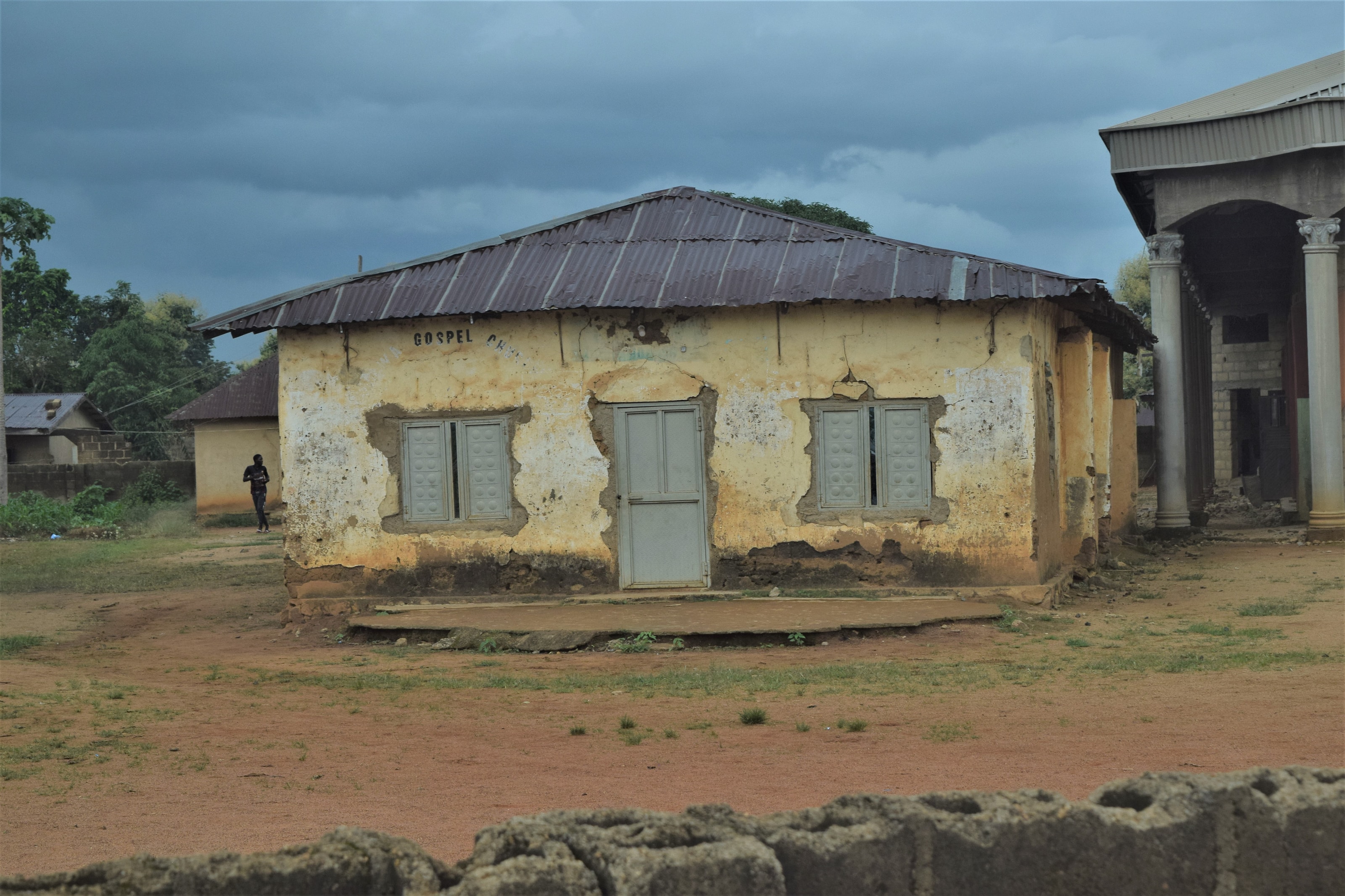 An old, weathered mud-walled church building with a corrugated roof, marked Gospel Church, at Kafanchan in southern Kaduna, Nigeria