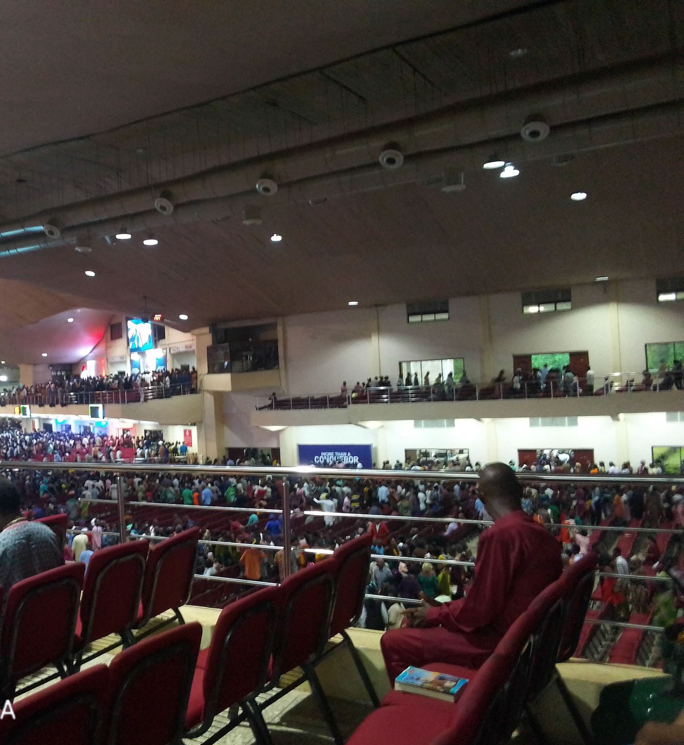 View from an upper gallery over a vast church auditorium filled with worshipers seated in red chairs