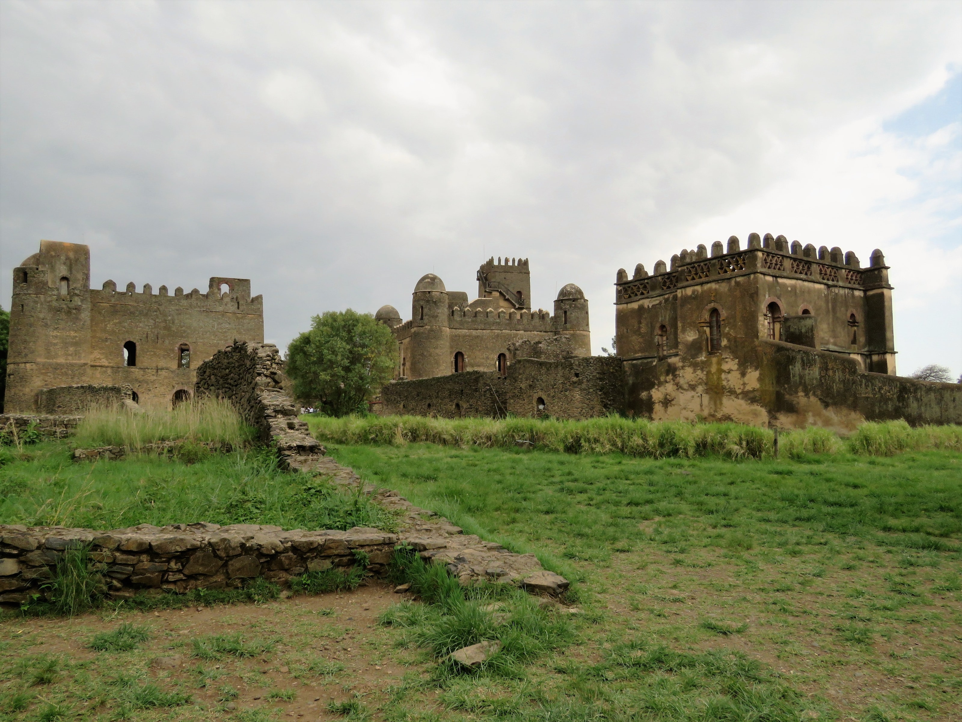 Stone castles with crenellated towers in a grassy royal compound at Gondar under a cloudy sky