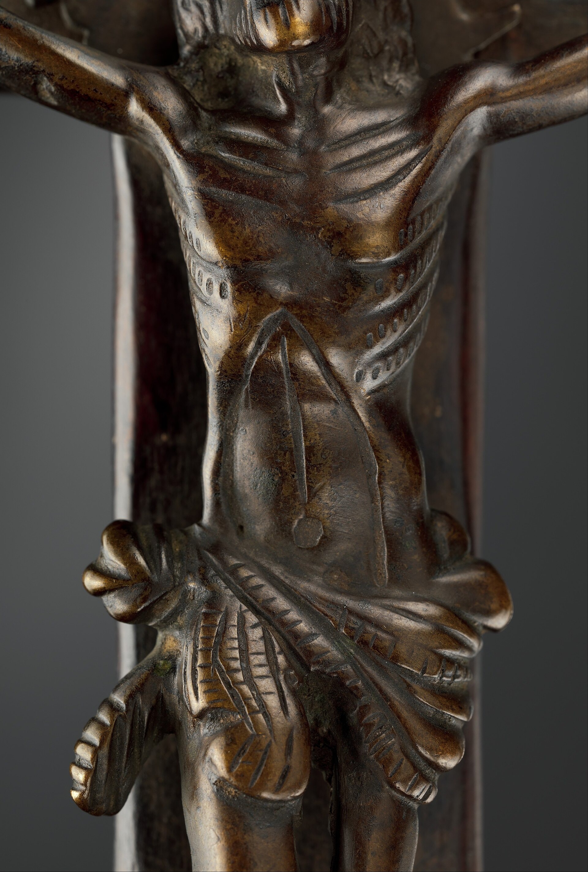 Close view of a dark brass crucifix figure of Christ with a patterned loincloth, mounted on a wooden cross