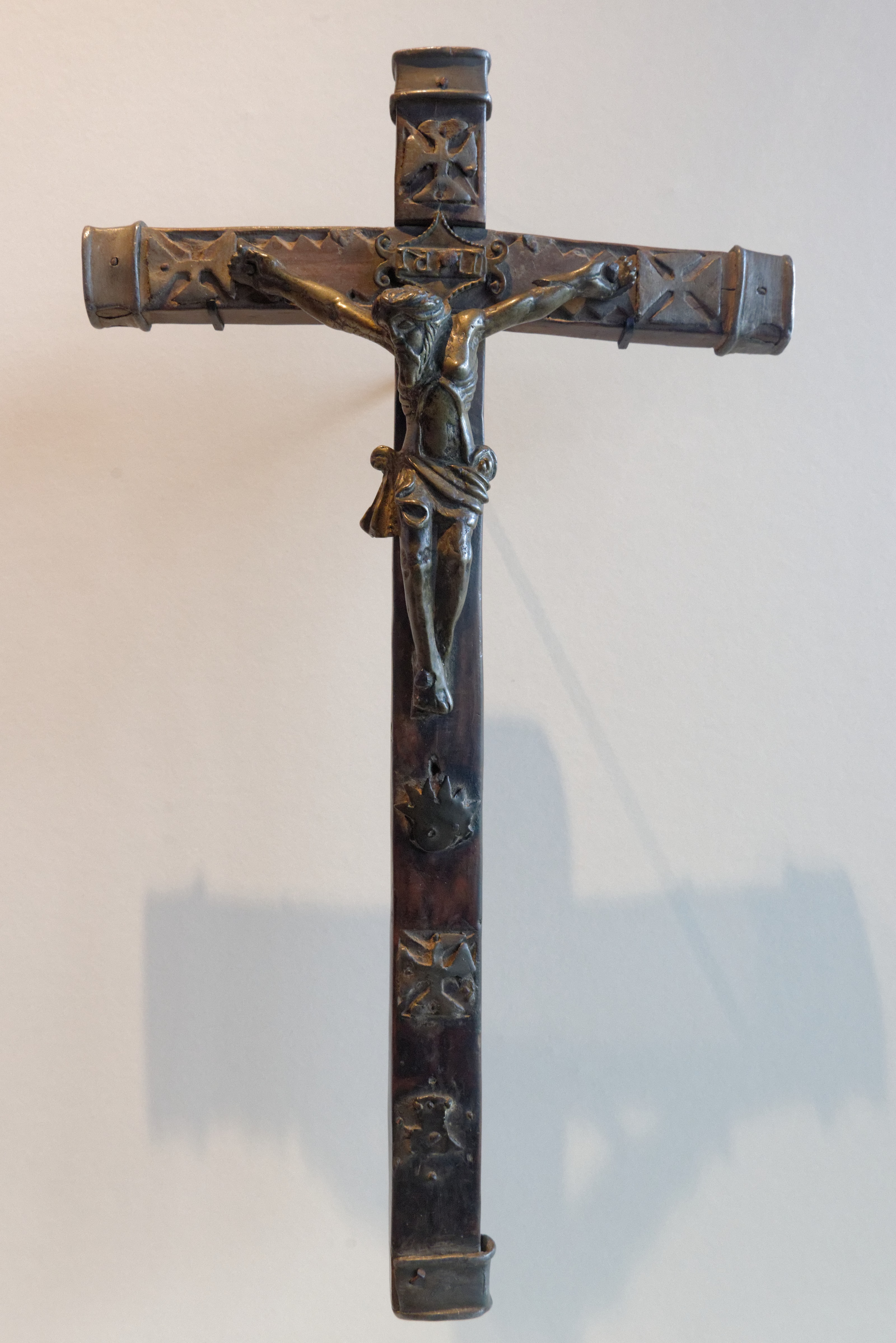 A Kongo crucifix of dark wood with a cast brass figure of Christ and small brass plaques along the arms and shaft