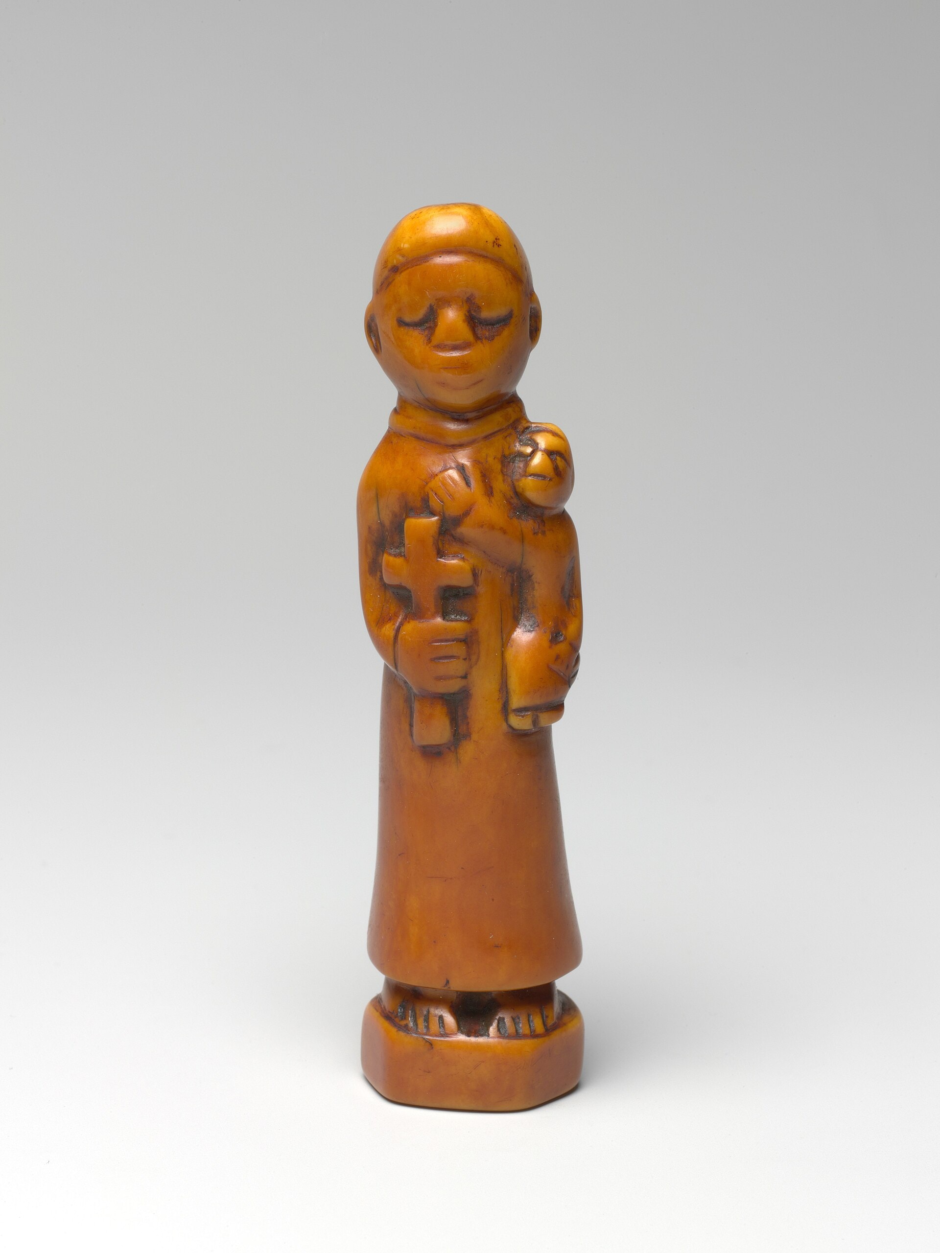 A small carved ivory figure of a robed friar holding a cross in one hand and the Christ child in the other, made in the Kingdom of Kongo