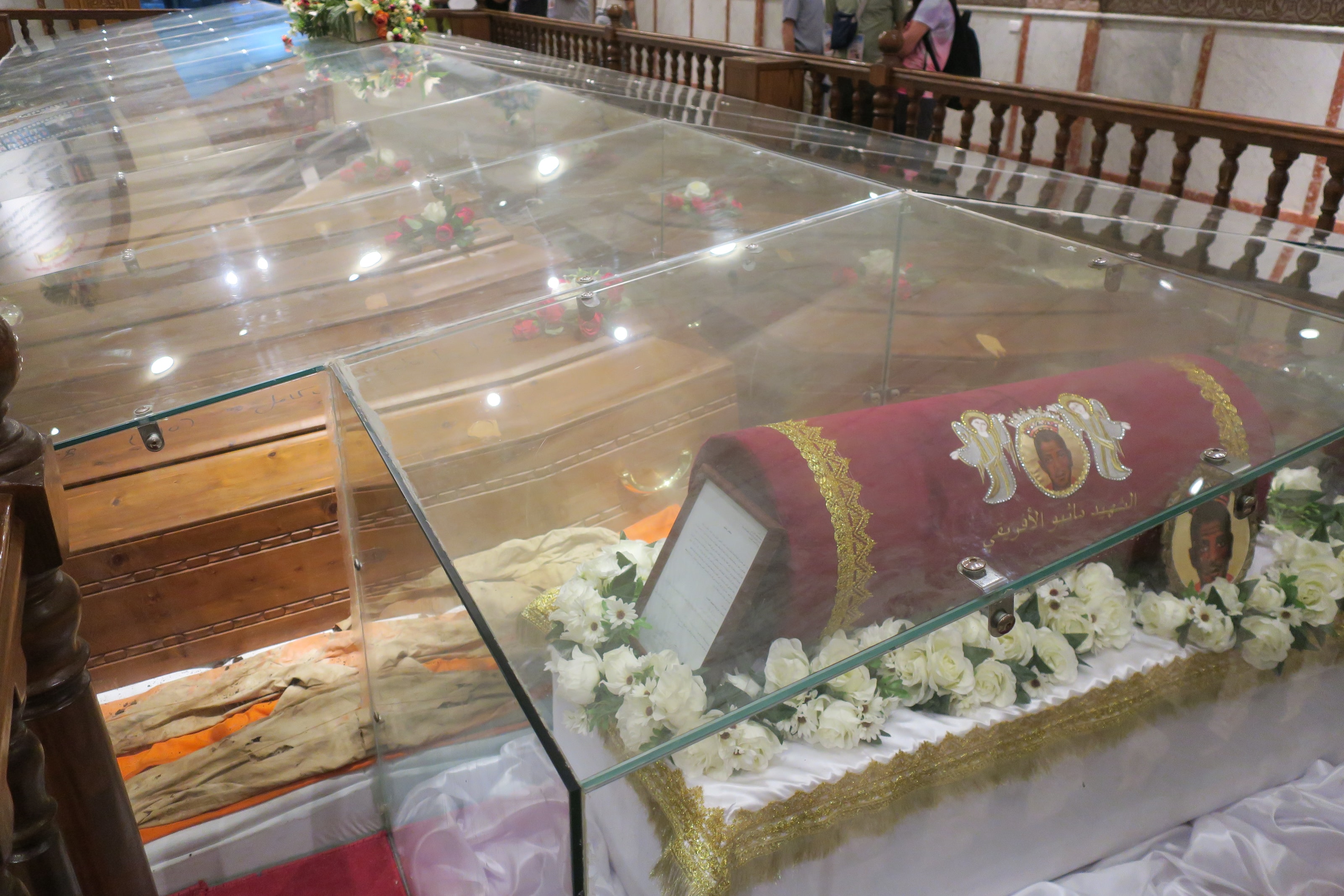 Glass-topped reliquary caskets draped in red and gold cloth with white flowers inside a church