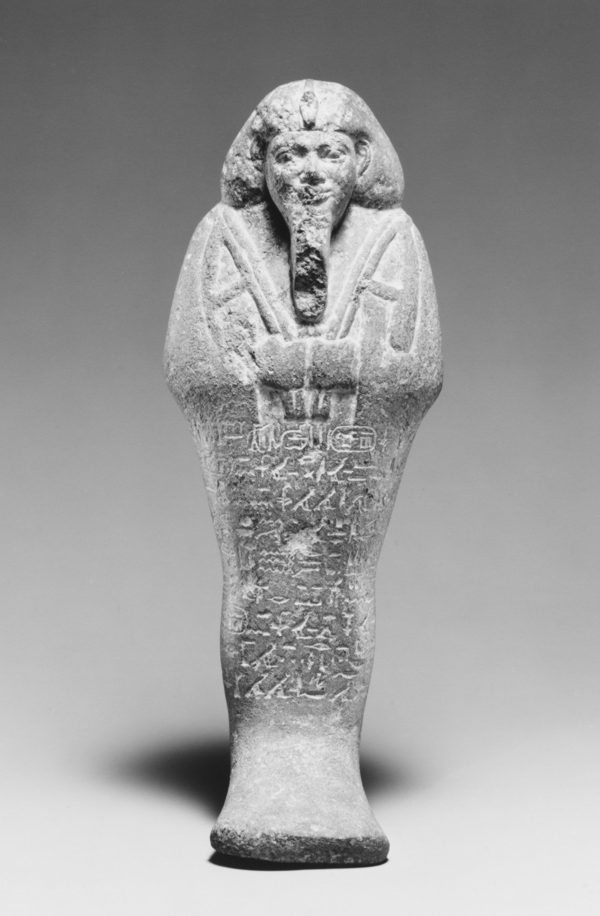A stone funerary figurine of King Taharqa in mummy form, wearing a royal headdress and false beard, its body inscribed with hieroglyphs